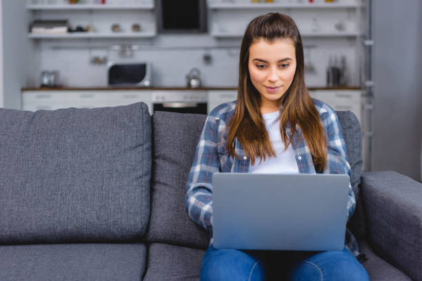 istock beautiful smiling young woman sitting on couch and using laptop 1078413890