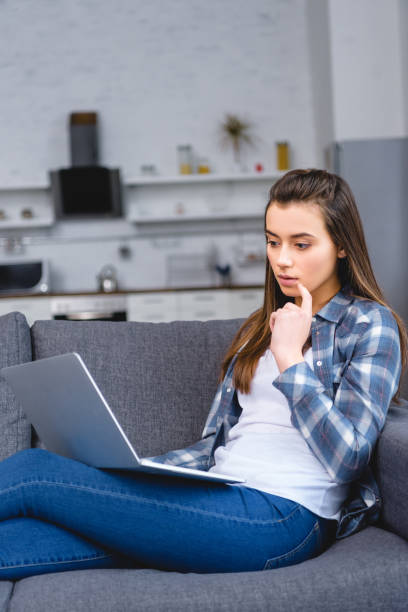 istock thoughtful young woman sitting on couch and using laptop 1078413894