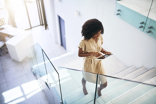 Shot of a young businesswoman using a digital tablet while walking up a staircase in an office