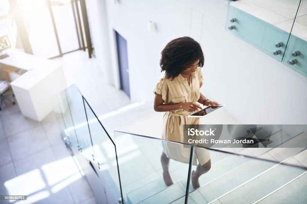 Technology helps her step up her business game Shot of a young businesswoman using a digital tablet while walking up a staircase in an office Staircase Stock Photo