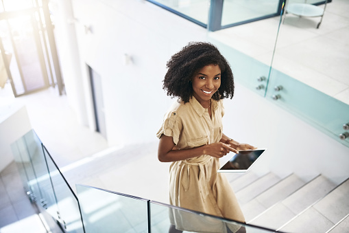 Portrait of a young businesswoman using a digital tablet while walking up a staircase in an office