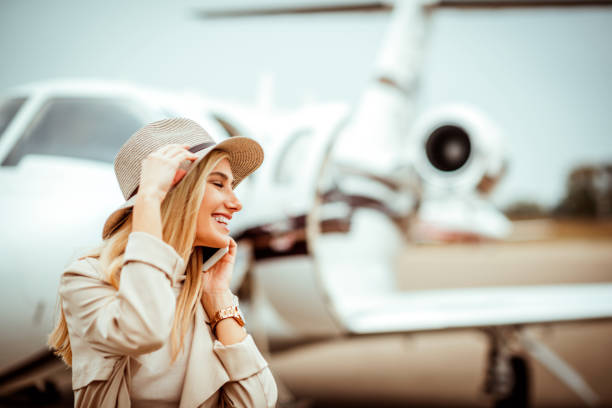 istock Young beautiful blond model having a phone conversation near a private jet on a runway 1078448198