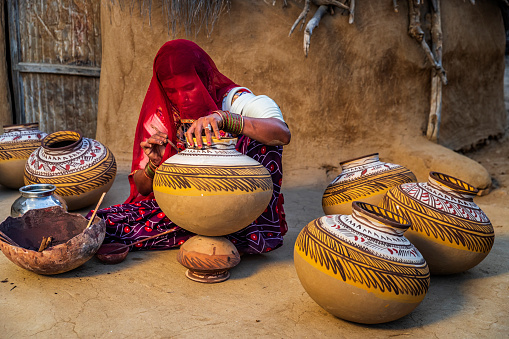 Indian woman painting water pots in her workshop, desert village in Rajasthan, India