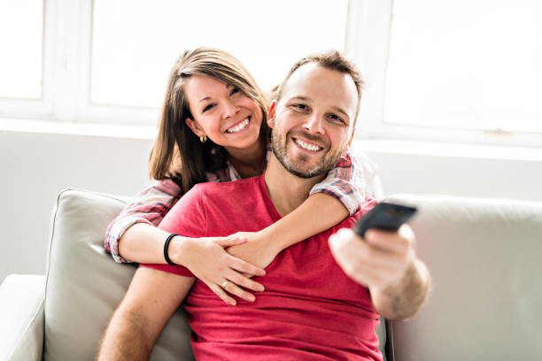 istock Couple sitting together on sofa at home with remote control tv 1078460306