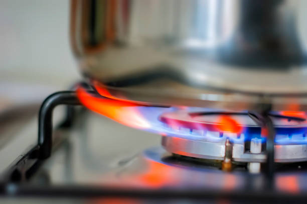 A close-up image of a gas stove burner, featuring bright blue flames encircling the burner, creating a vibrant display of heat and power.