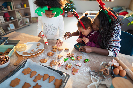 Young African - American woman and her daughters decorating gingerbread cookies for Christmas together and having fun.