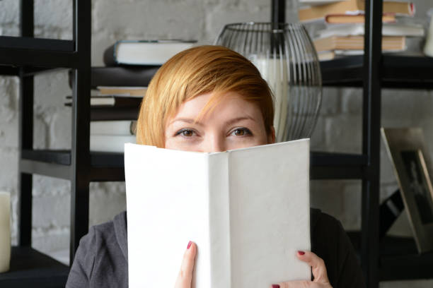 istock Pretty young woman peeking out cheerfully from behind a book 1078480958