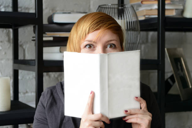 istock Pretty young woman peeking out cheerfully from behind a book 1078480960