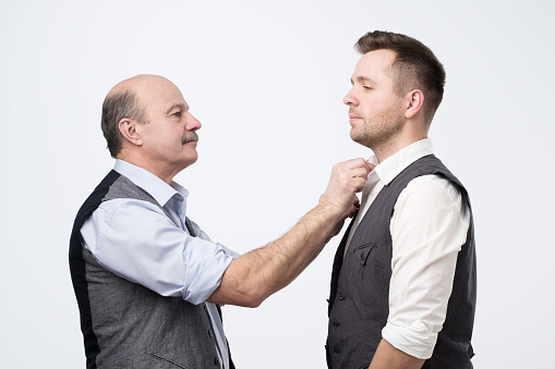 Senior father help his mature son with clothes shir before wedding. Studio shoot