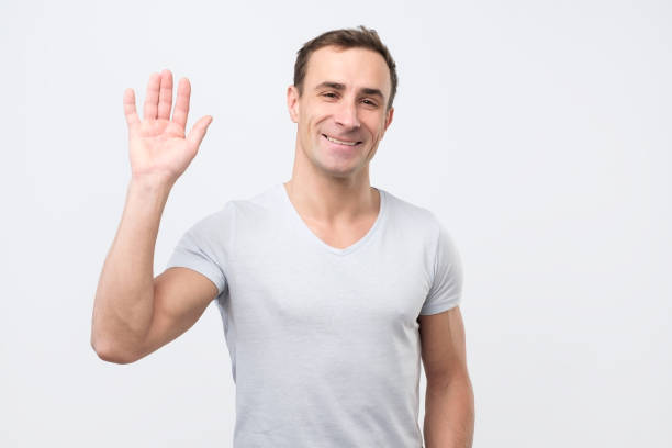 istock Friendly looking attractive males waives hand in hello gesture while smiling cheerfully 1078484274