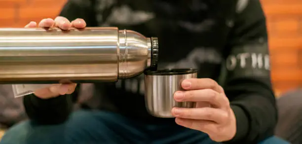 Photo of adult man pour tea and coffee in the cup from thermos at home f