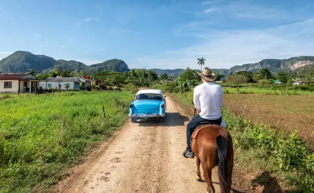 A classic car passes a man on horse in Vinales, Cuba.