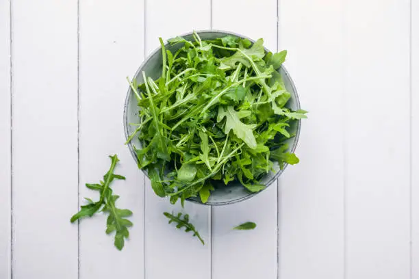 Bowl with fresh green salad arugula rucola on a wooden Black or White background