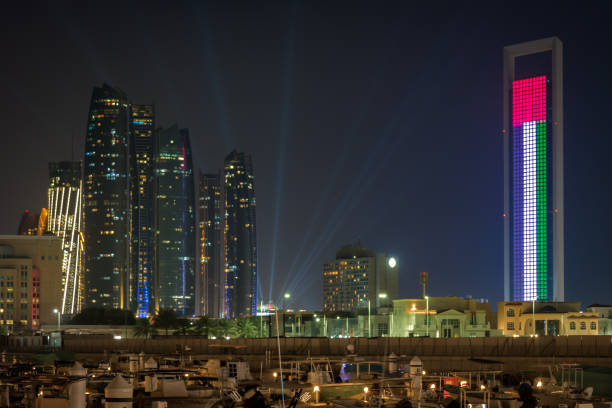 splendida vista del famoso paesaggio della città di abu dhabi che mostra bandiera degli emirati arabi uniti, torri etihad e barche marina di notte - dubai yacht luxury marina foto e immagini stock