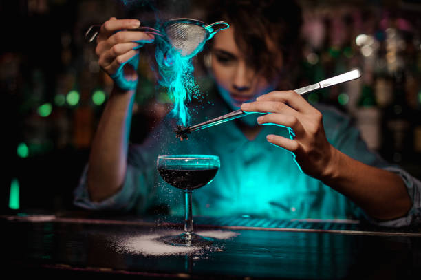 mujer bartender verter el cóctel marrón y una badiana flameado en pinzas de azúcar en la luz verde - badian fotografías e imágenes de stock