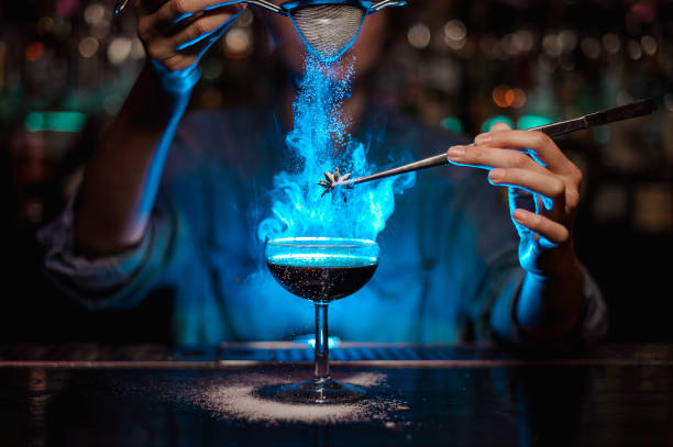 Bartender girl adding to a brown cocktail and pour on a flamed badian on tweezers a powdered sugar in the blue light Bartender girl adding to a brown cocktail and pour on a flamed badian on tweezers a powdered sugar on the bar counter in the blue light. bartender stock pictures, royalty-free photos & images