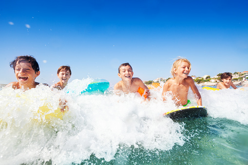 Close-up portrait of happy teenage boys riding the waves on body boards in summer