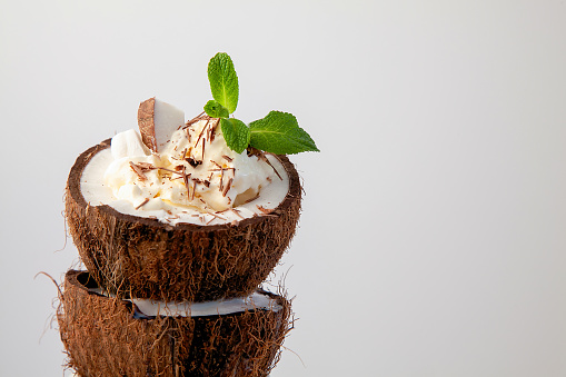 ice cream decorated with chocolate chips and mint in coconut shell on white background.Object on left
