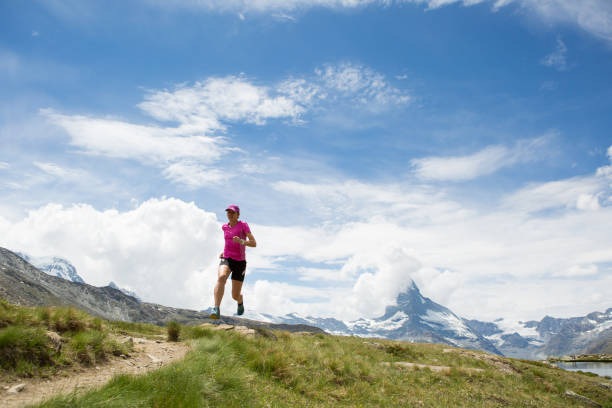 Fit woman runs along a mountain path in Switzerland, the Matterhorn lies in the background
