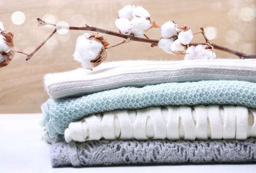 Stack  knitted clothes with cotton flower branch,woolen clothing.Pile of winter sweaters pastel colored.