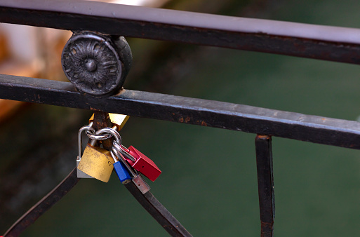 group of padlocks hooked to the railing of a bridge, of different colors, red, blue, yellow and metallic grar. Conceptual photo of love and commitment, as background the water in green tone