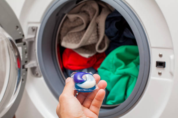 Laundry detergent pod Close up picture of person holding laundry detergent 3 in 1 pod capsule, washing machine with laundry in the background detergent capsule stock pictures, royalty-free photos & images