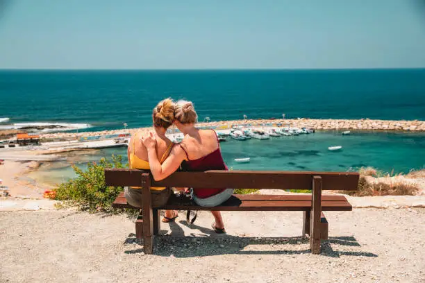 Mature female couple sitting down outside overlooking the sea in Paphos, Cyprus. They are spending quality time together and looking at the view.