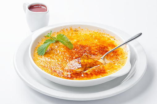 French dessert creme brulee with berry sauce and mint in a white plate