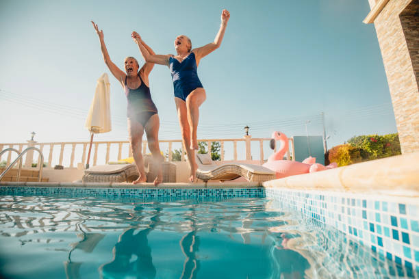 Young at Heart Two senior women holding hands and jumping into a swimming pool. They're excited and having fun. republic of cyprus photos stock pictures, royalty-free photos & images