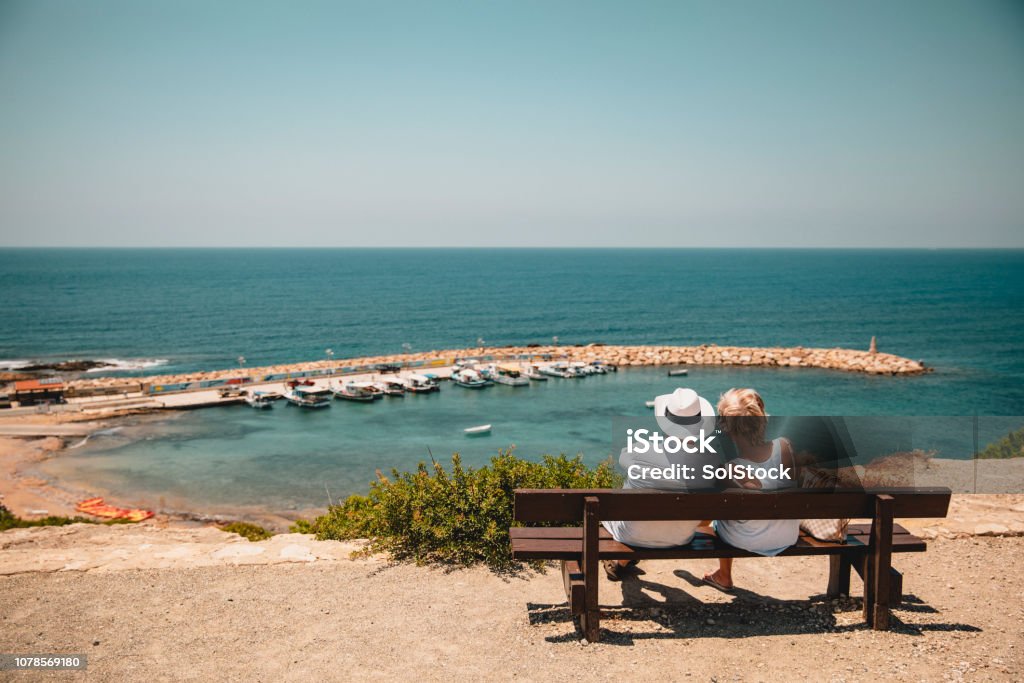 Senior Couple Enjoying the View Senior couple sitting down on a bench overlooking the Mediterranean Sea. They are relaxing and spending time together. Republic Of Cyprus Stock Photo
