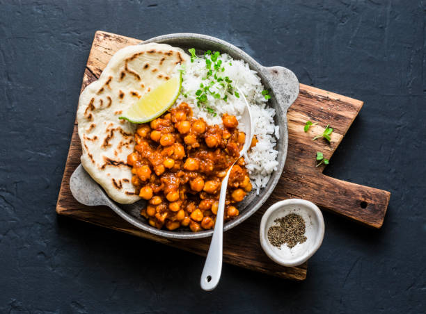 indische würzige kichererbsen curry mit reis und naan brot in pfanne auf dunklem hintergrund, ansicht von oben. gesunde leckere vegetarische kost - indische gerichte stock-fotos und bilder