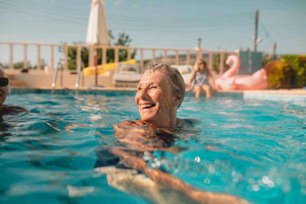 Senior woman swimming in a swimming pool while on holiday in Paphos, Cyprus. She is turning her head as she swims to laugh at her friends.