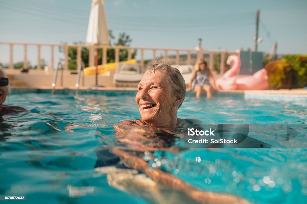 Senior Woman Enjoying Summer Vacation Senior woman swimming in a swimming pool while on holiday in Paphos, Cyprus. She is turning her head as she swims to laugh at her friends. Senior Adult Stock Photo