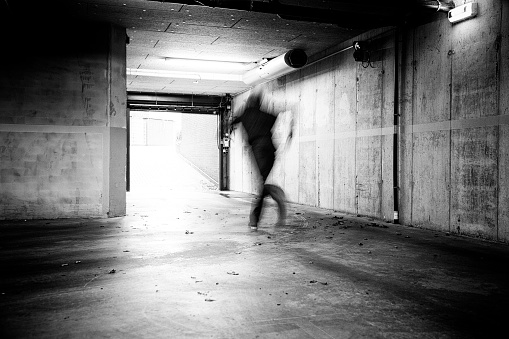 Monochrome of a man fleeing a grungy underground parking.