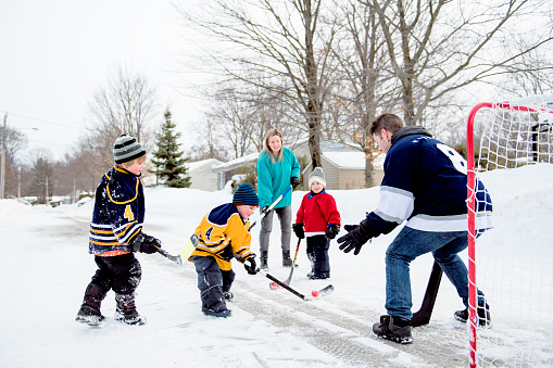 Niños graciosos felices jugando al hockey con padre y madre en la calle en invierno photo