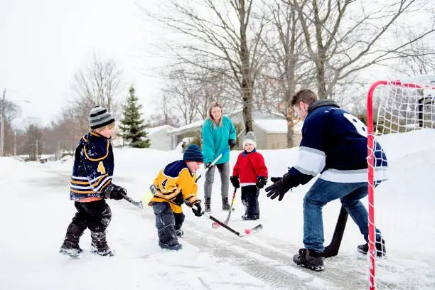 Photo of Happy funny kids playing hockey with father and mother on street in the winter season