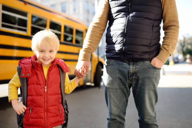 istock Elementary student hold hands his father near yellow school bus on background. 1078624648