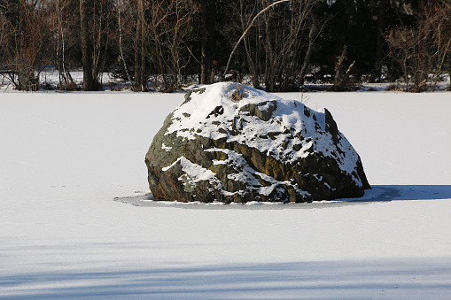 A boulder rests at the edge of a lake in Southern Quebec.  A new snowfall covers it partially.