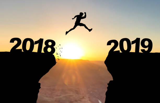 istock Man jumping over abyss in front of sunset with text 2018/2019 1078633636