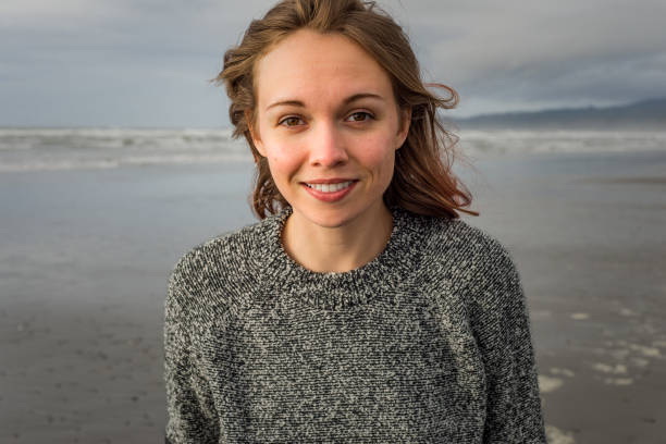 Young woman standing on a beach, looking at the camera and smiling stock photo
