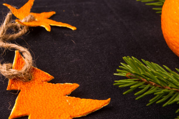New Year Concept. Christmas decorations from tangerine peel, fir-tree branches and the fruits of mandarin orange on black background