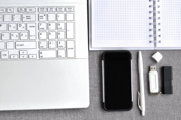 bem acima vista do local de trabalho de escritório com telefone móvel e portátil perto teclado de computador com caderno, caneta e usb flash na mesa cinza. conceito de mesa de mesa de blogging de trabalho - mobile office flash - fotografias e filmes do acervo