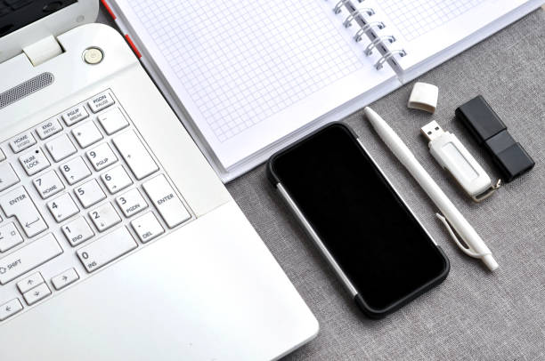 bem acima vista do local de trabalho de escritório com telefone móvel e portátil perto teclado de computador com caderno, caneta e usb flash na mesa cinza. conceito de mesa de mesa de blogging de trabalho - mobile office flash - fotografias e filmes do acervo