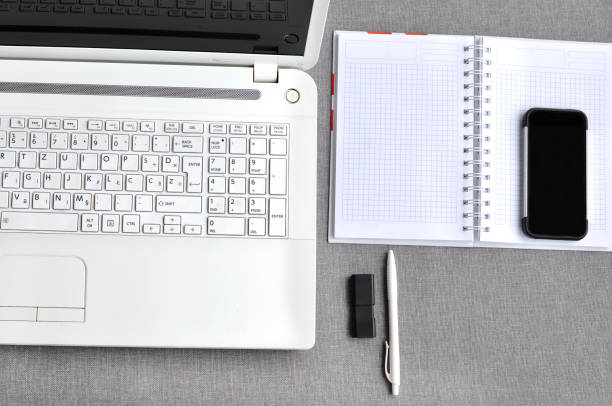 bem acima vista do local de trabalho de escritório com telefone móvel e portátil perto teclado de computador com caderno, caneta e usb flash na mesa cinza. conceito de mesa de mesa de blogging de trabalho - mobile office flash - fotografias e filmes do acervo