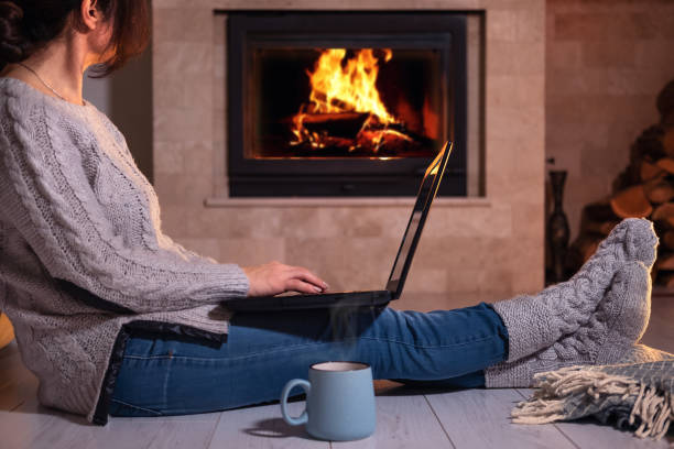 freelancer jeune femme assise au sol avec un ordinateur portable sur le fond de la cheminée. - blanket fireplace winter women photos et images de collection