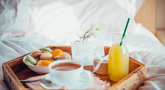 Breakfast in bed with i love you text on a note. Cup of coffee, juice, macaroons, rose and giftbox on wooden tray. Romantic breakfast in bed. Birthday, Valentine's day morning. Wide banner. Copy space.