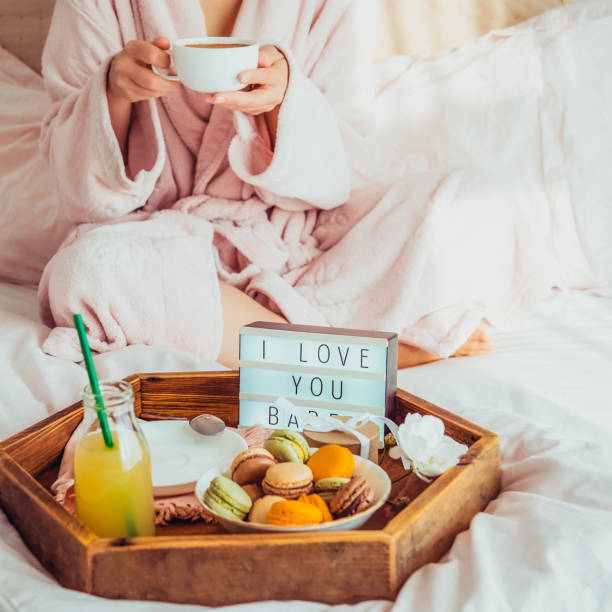 istock Romantic Breakfast in bed with I love you text on lighted box, macaroons, gift box on wooden tray and blurred cropped woman in a bathrobe drinking her coffee. Birthday, Valentine's day morning. Square 1078667650
