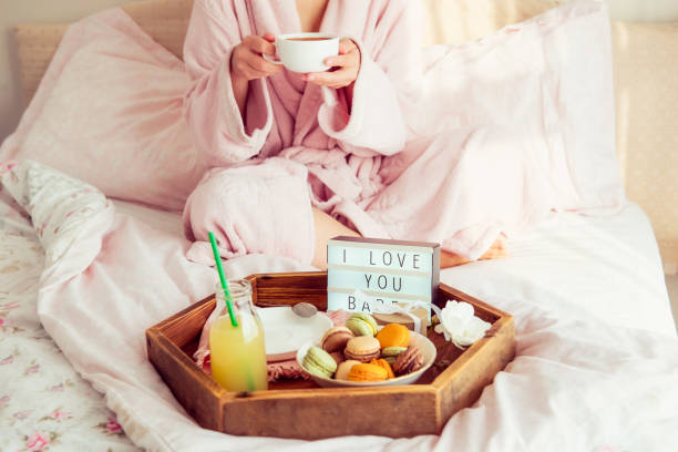 istock Romantic Breakfast in bed with I love you text on lighted box, macaroons, gift box on wooden tray and blurred cropped woman in a bathrobe drinking her coffee. Birthday, Valentine's day morning. 1078667658