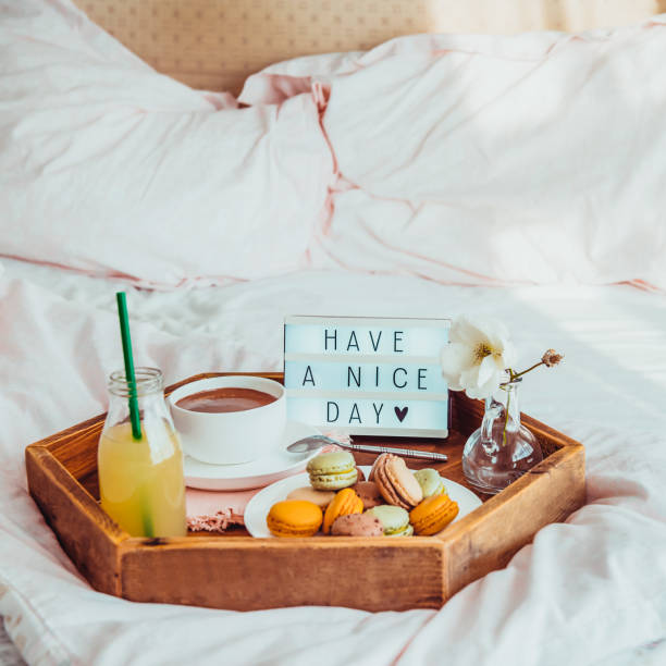 istock Breakfast in bed with Have a nice day text on lighted box. Cup of coffee, juice, macaroons, flower in vase on wooden tray. Good morning mood. Hospitality, care, service concept. Square. Copy space. 1078667660