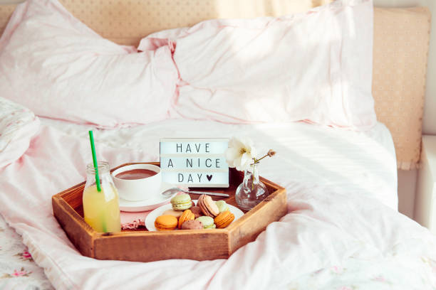 istock Breakfast in bed with Have a nice day text on lighted box. Cup of coffee, juice, macaroons, flower in vase on wooden tray. Good morning mood. Hospitality, care, service concept. Copy space. 1078667678